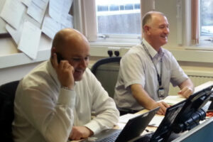 Two male civil servants working at desks in a commuter hub