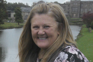 Sue Byrom with large pond and building behind