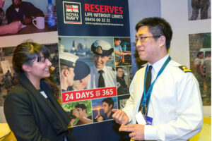 Royal Naval Reservist (right) explaining Reserve Forces to a female visitor at the Reserves Experience