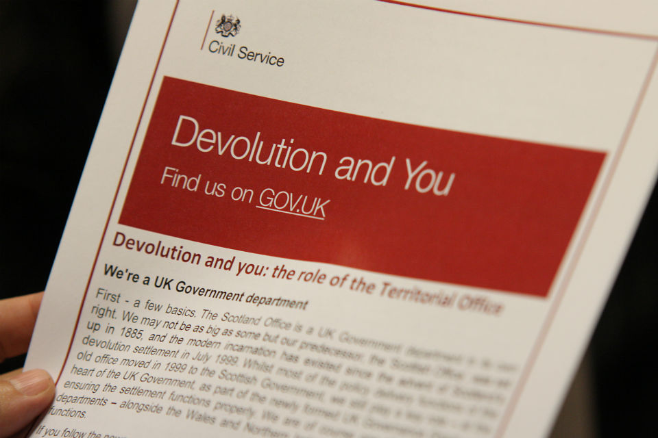 Tip of fingers of a hand holding booklet, showing title 'Devolution and You'