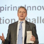 Jeremy Heywood speaking in front of screen with key words including, 'inspiring', 'innovative', 'challenge'