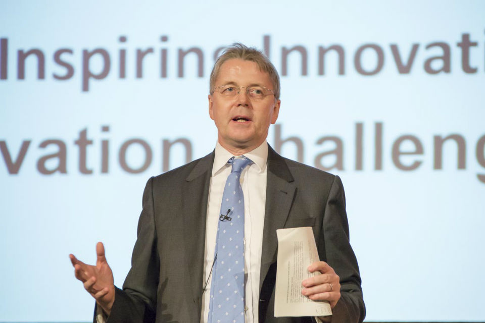 Jeremy Heywood speaking in front of screen with key words including, 'inspiring', 'innovative', 'challenge'