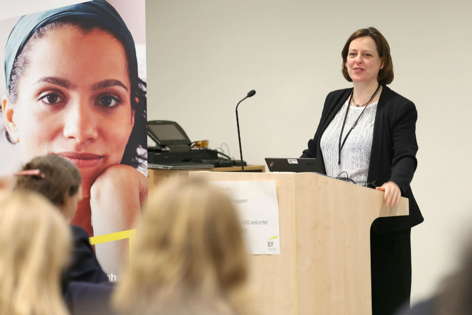 Melanie Dawes at lectern with large poster of woman in headscarf extreme left