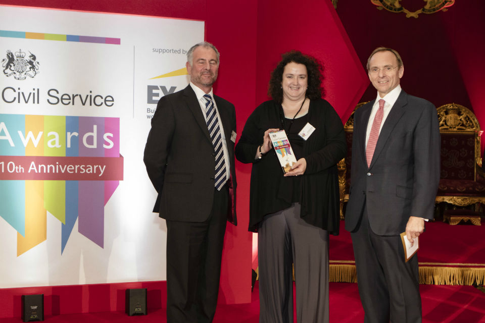 Woman with award flanked by two men with Civil Service Awards banner to their right