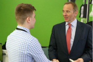 Young man in light blue and white checked shirt (left) shaking hands with bespectacled man in suit