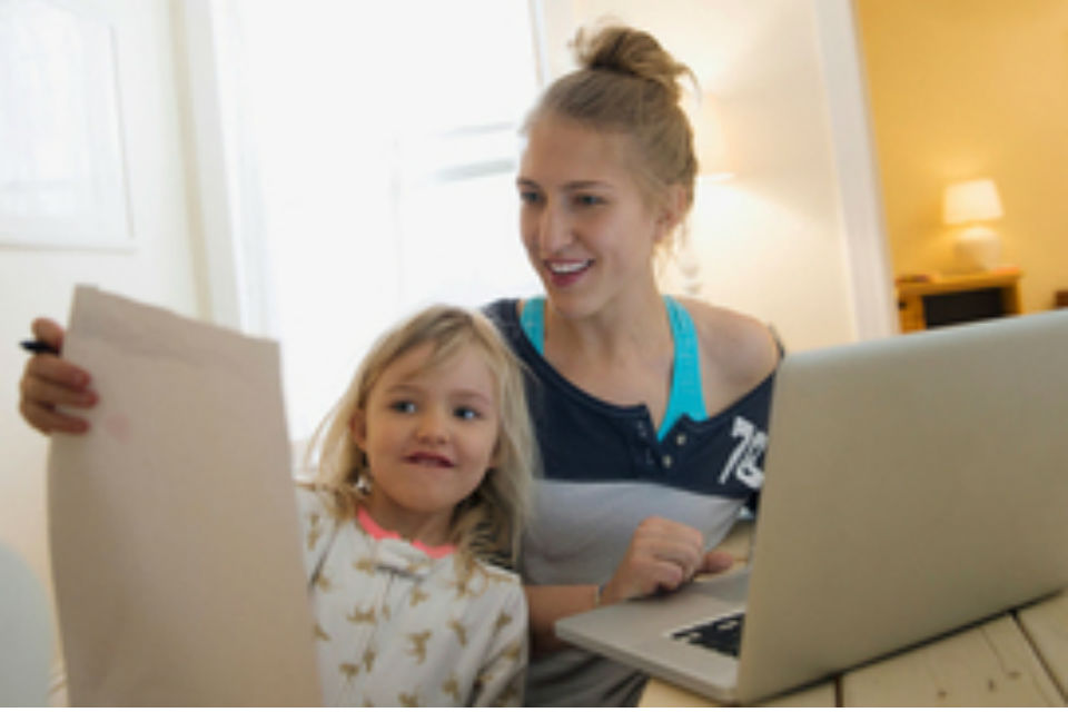 Young girl showing drawing to woman using laptop
