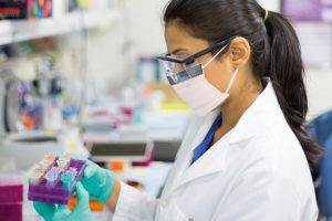 Female lab researcher with face mask and holding test tube tray