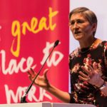 Woman speaking at lectern with banner behind with legend 'A great place to work'