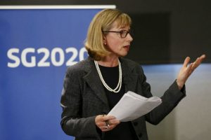 Woman in glasses speaking, with banner and legend SG2020 behind