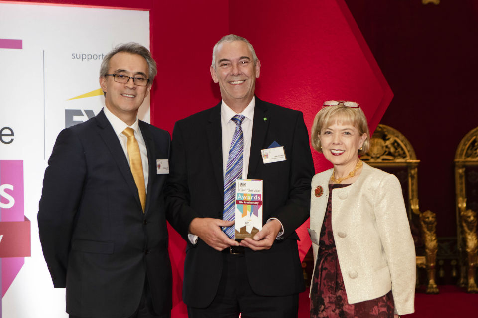 Man centre with award, flanked by man and woman