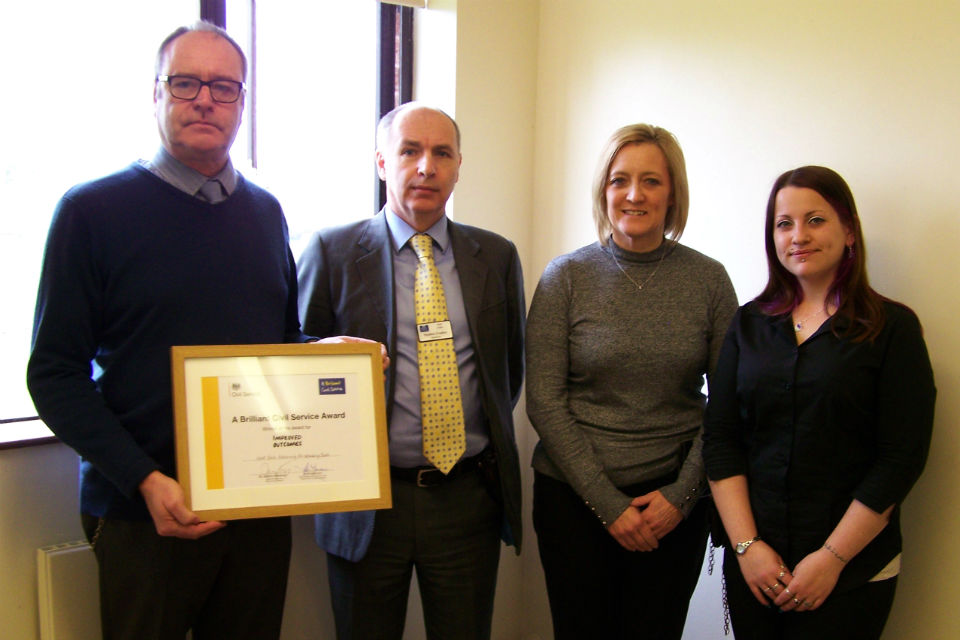 Two men and two women in a line, one holding framed award certificate