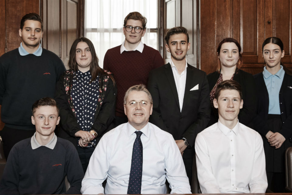 Group shot of man seated, centre, with school students behind and alongside