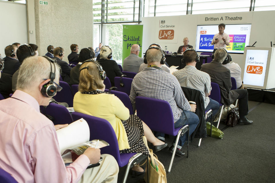 Presenter speaking from platform to seated audience at conference