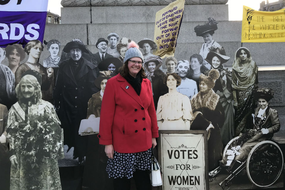 Woman in Trafalgar Square surrounded by cut-outs of women's suffrage campaigners