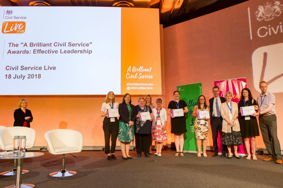 Group of men and women showing off award certificates on stage at conference