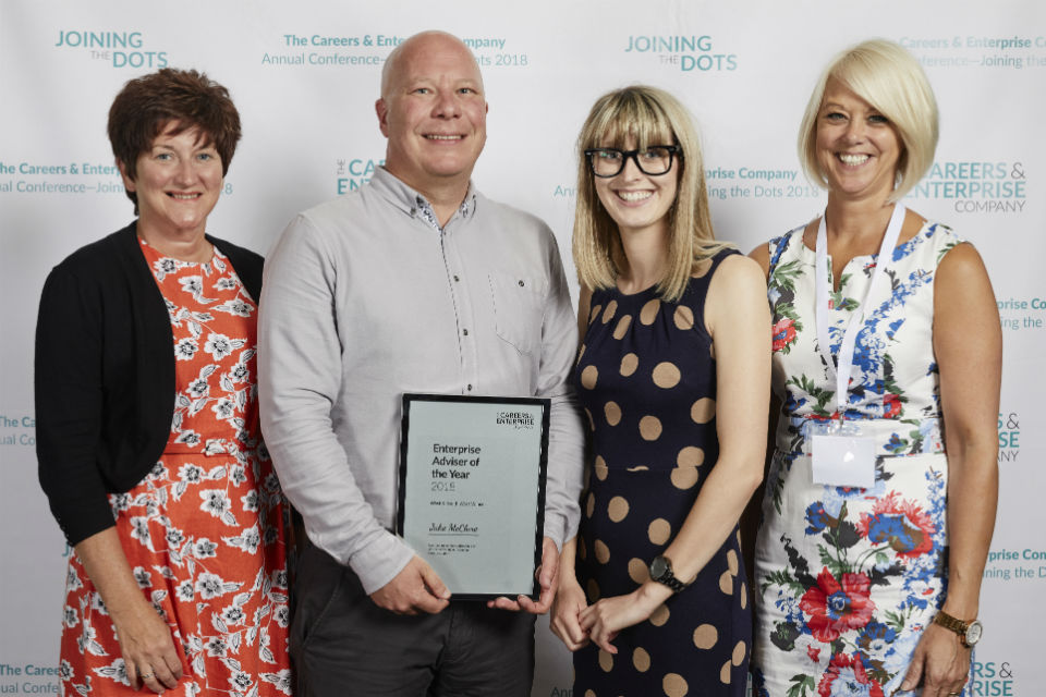 Man holding award flanked by three women presenters