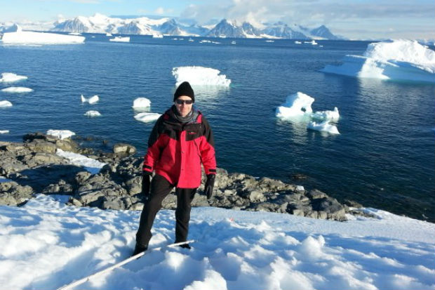 Ben Merrick pictured in Antarctica, dressed in cold-weather gear and with the sea and icebergs in the background.