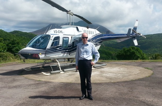 Ben Merrick on a helicopter landing pad in Montserrat, with a helicopter behind him