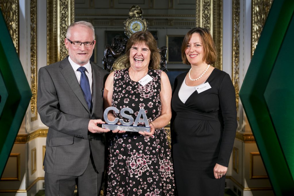 Mairi Macneil, holding her Citizenship Award, flanked by two award presenters