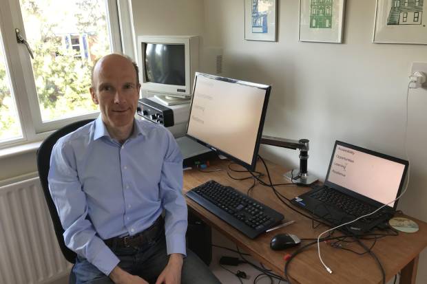 Ben Merrick seated in front of his desk and IT equipment in his home